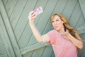 Image showing Young Adult Woman Wearing Earphones Taking a Selfie with Her Sma
