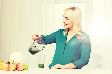 Image showing happy woman with blender jug pouring juice at home