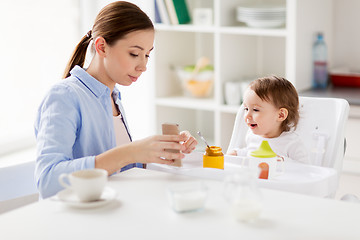 Image showing mother with smartphone and baby eating at home 