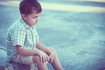 Image showing Portrait of sad little boy sitting on street