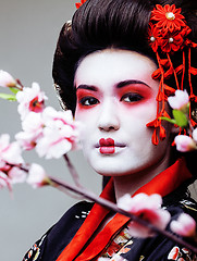 Image showing young pretty geisha in black kimono among sakura, asian ethno close up