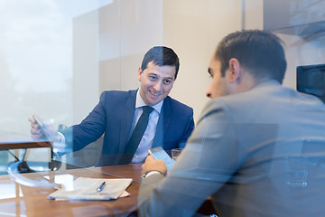 Image showing Two young businessmen using smart phones and touchpad at meeting.