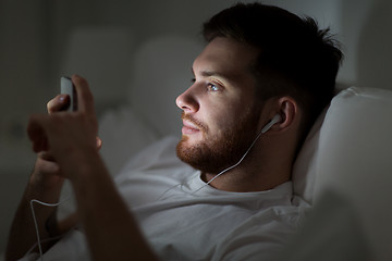 Image showing man with smartphone and earphones in bed at night