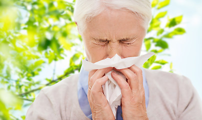 Image showing sick senior woman blowing nose to paper napkin