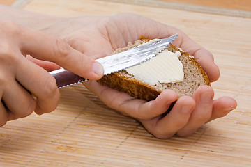 Image showing woman hands spreading butter on piece of rye bread