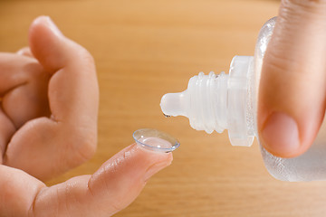 Image showing hands washing contact lens with solution