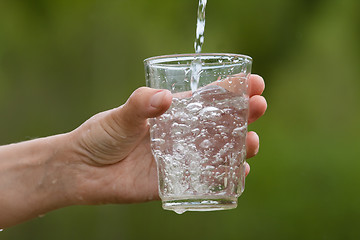Image showing hand pouring clean natural water into a glass, closeup