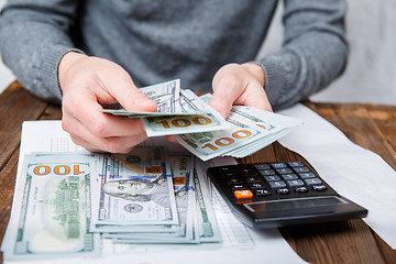 Image showing Caucasian hands counting dollar banknotes on dark wooden table