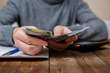 Image showing Caucasian hands counting dollar banknotes on dark wooden table