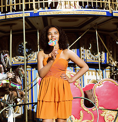 Image showing cool real teenage girl with candy near carousels at amusement pa