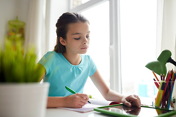 Image showing girl with tablet pc writing to notebook at home