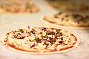 Image showing raw pizza with grated cheese on table at pizzeria