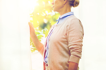 Image showing lonely senior woman looking through window at home