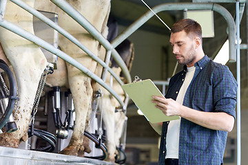 Image showing man with clipboard and milking cows on dairy farm