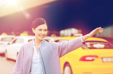 Image showing smiling young woman waving hand and catching taxi