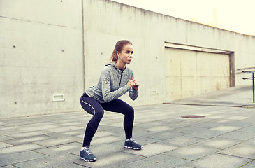 Image showing happy woman doing squats and exercising outdoors