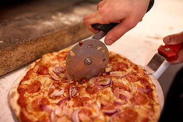 Image showing cook hands cutting pizza to pieces at pizzeria