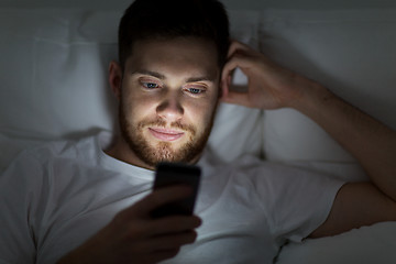 Image showing young man with smartphone in bed at night