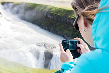 Image showing Woman photographing a waterfall with a mobile phone