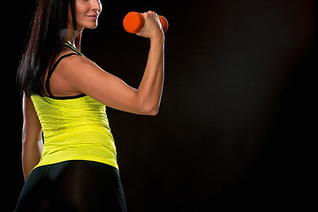 Image showing The woman training against black studio with red dumbbells