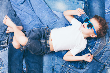 Image showing Cute little boy with sunglasses on the background jeans. 