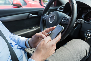 Image showing Businessman texting on his mobile phone while driving.