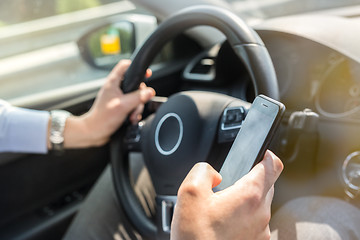 Image showing Businessman texting on his mobile phone while driving.