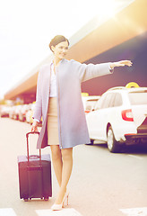 Image showing smiling young woman with travel bag catching taxi