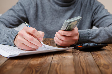 Image showing Caucasian hands counting dollar banknotes on dark wooden table