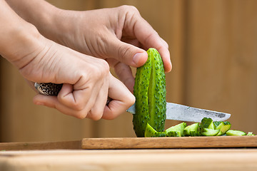 Image showing hands cutting cucumber on the wooden cutting board