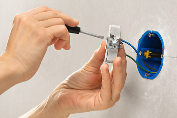 Image showing hands installing electrical wall socket with screwdriver