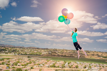 Image showing Young Girl Being Carried Up and Away By Balloons That She Is Hol