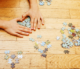 Image showing little kid playing with puzzles on wooden floor together with pa