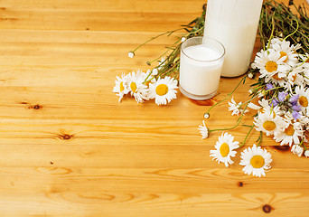 Image showing Simply stylish wooden kitchen with bottle of milk and glass on table, summer flowers camomile, healthy foog moring concept