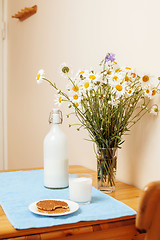 Image showing Simply stylish wooden kitchen with bottle of milk and glass on table, summer flowers camomile, healthy foog moring concept