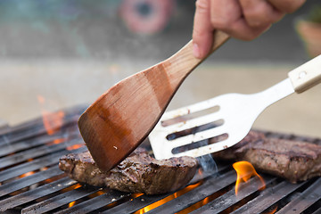 Image showing Chef grilling beef steaks on open flame BBQ.