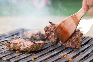 Image showing Chef grilling beef steaks on open flame BBQ.