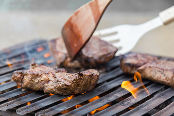 Image showing Chef grilling beef steaks on open flame BBQ.