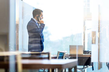 Image showing Businessman talking on a mobile phone while looking through window in NY