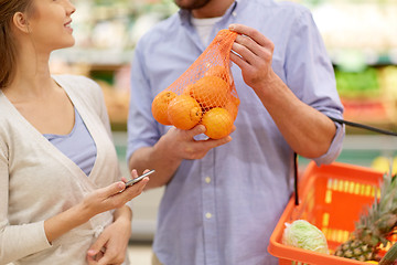 Image showing couple with smartphone buying oranges at grocery