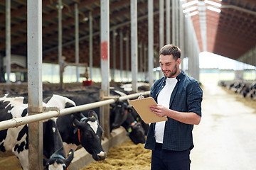 Image showing farmer with clipboard and cows in cowshed on farm