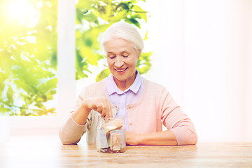 Image showing senior woman putting money into glass jar at home