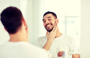 Image showing happy man applying aftershave at bathroom mirror