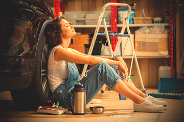 Image showing woman a car mechanic sits in a blue overall in a garage near a c