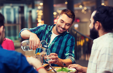 Image showing happy man with friends pouring water at restaurant