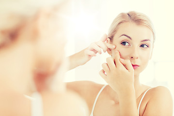 Image showing woman squeezing pimple at bathroom mirror