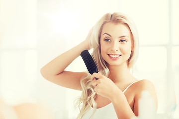 Image showing happy woman brushing hair with comb at bathroom