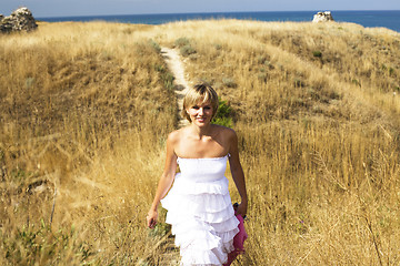 Image showing portrait of beautiful blond woman in white dress standing on wind with scarf near sea