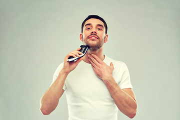 Image showing smiling man shaving beard with trimmer over gray