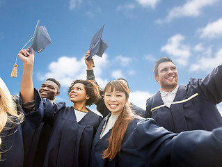 Image showing happy bachelors waving mortar boards over sky